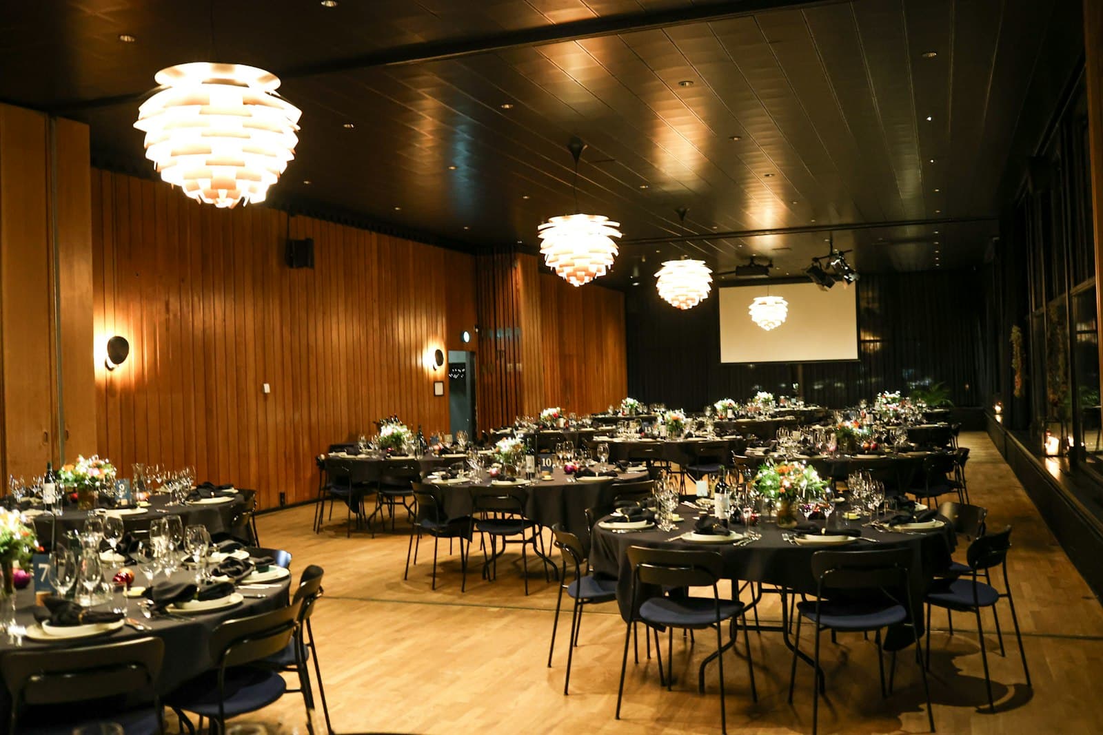 Salão de eventos com mesas redondas postas e luminárias pendentes